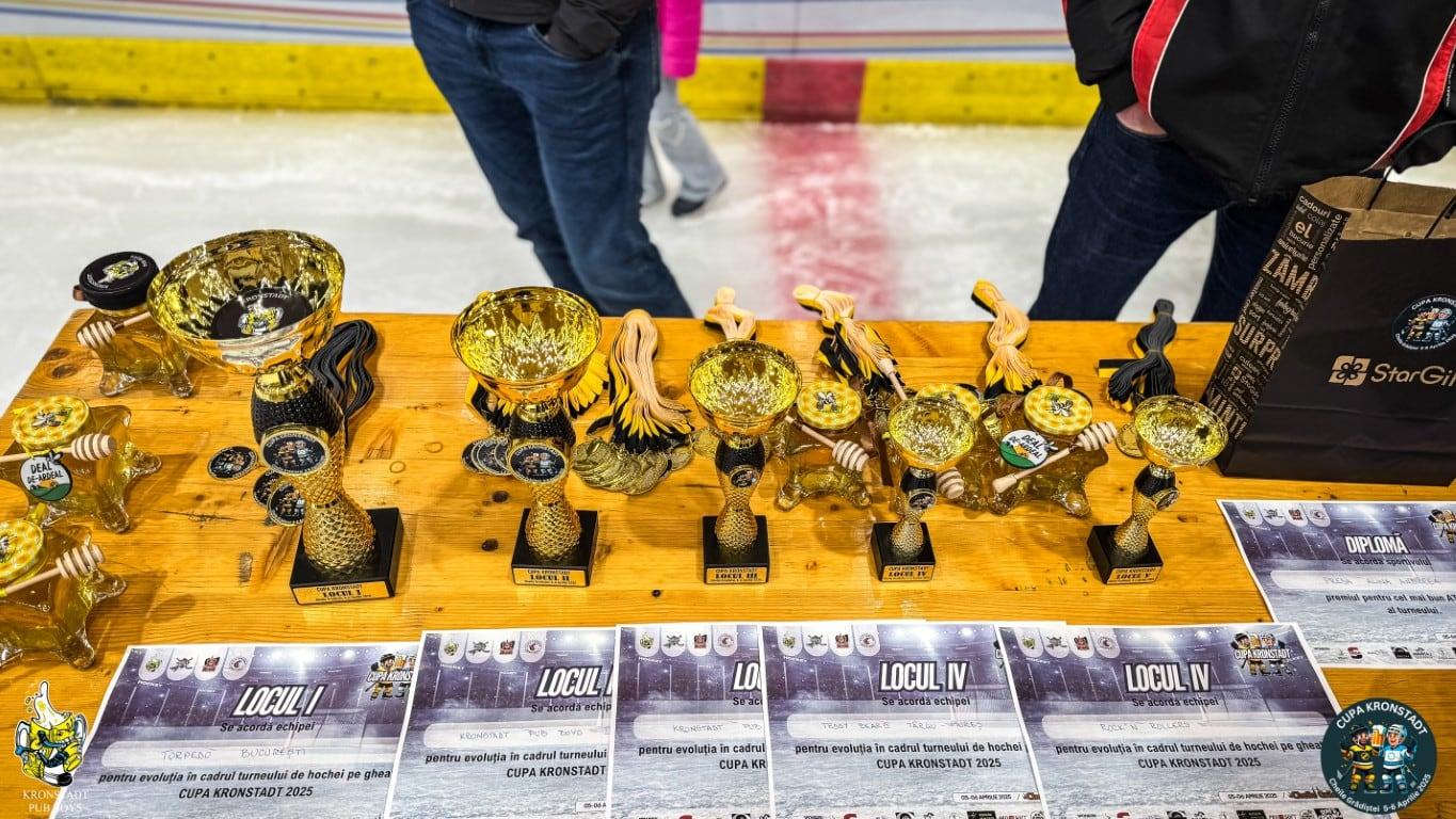 Trofeele, medaliile și diplomele turneului pe o masă lângă patinoar