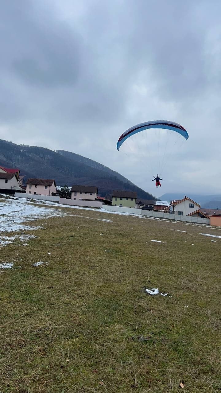 Pilot în zbor la mică înălțime deasupra pășunii, lângă sat