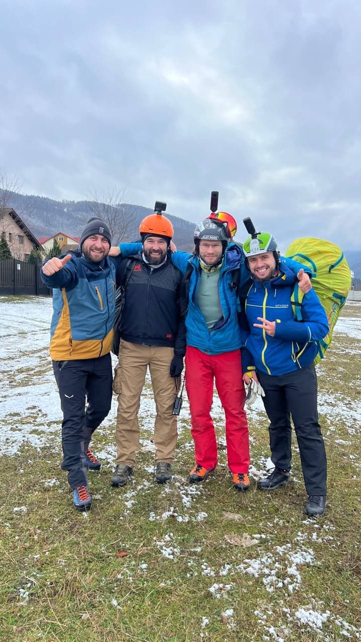 Patru piloți zâmbitori, cu căștile pe cap, pe dealul de zbor